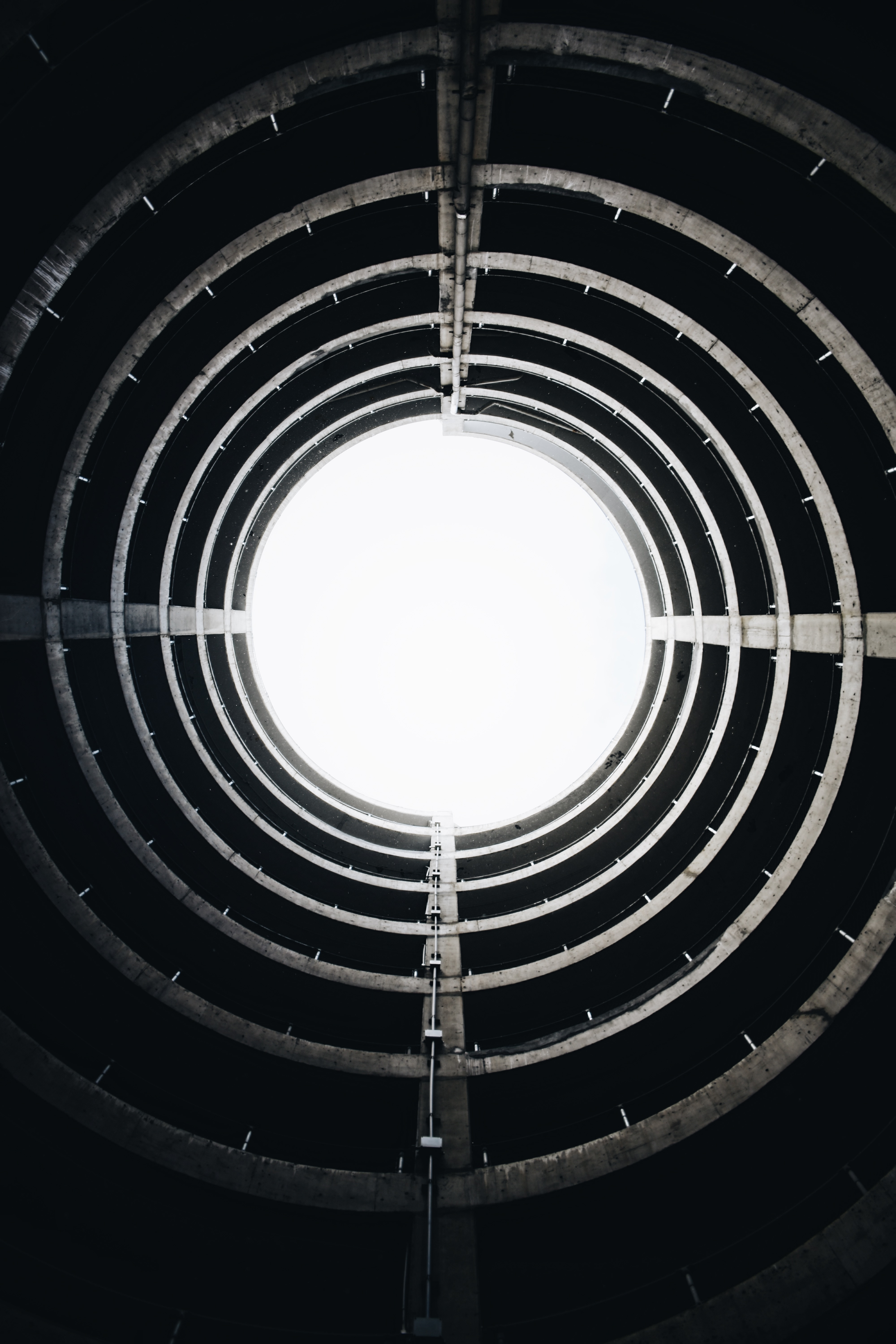 Fotografia em preto e brando de um prédio redondo, mostrando apenas a sua estrutura de concreto e tubulação. Como a foto é batida de dentro para fora, a sensação é estar dentro de um túnel com uma luz clara que indica a saída, ou mesmo a parte interna de um cano de um revólver.