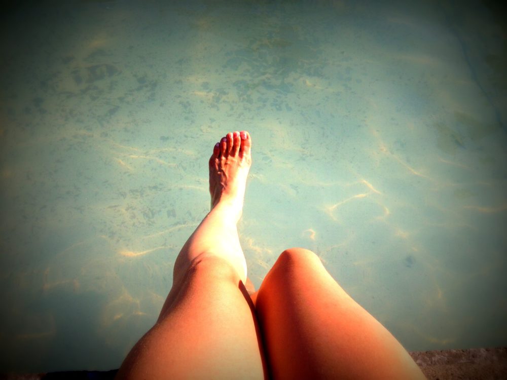 Pernas de uma mulher sentada na beirada de uma piscina.