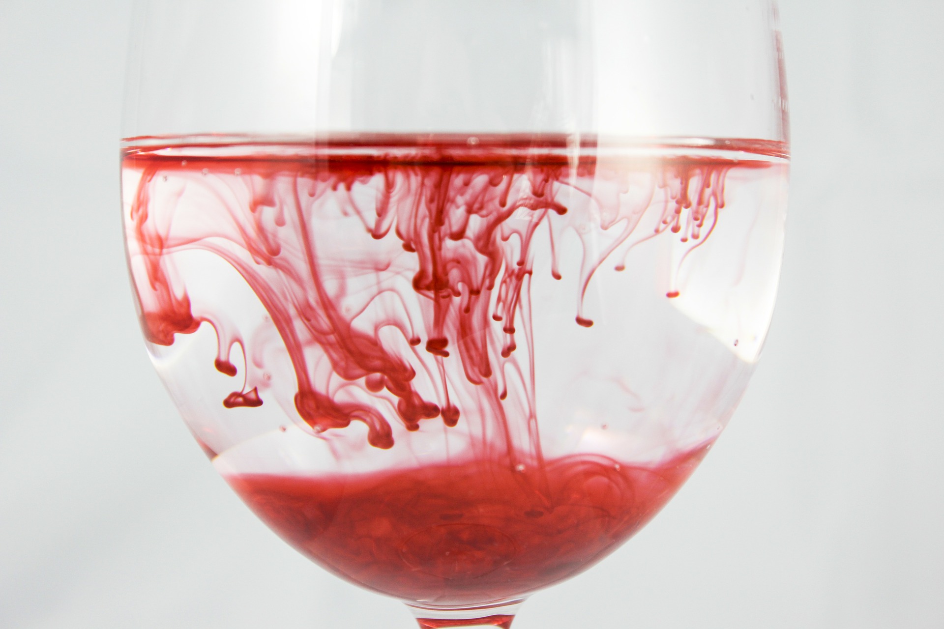 Imagem de uma taça de cristal com água, tingida por um pigmento vermelho, que parece se espalhar aos poucos no conteúdo.