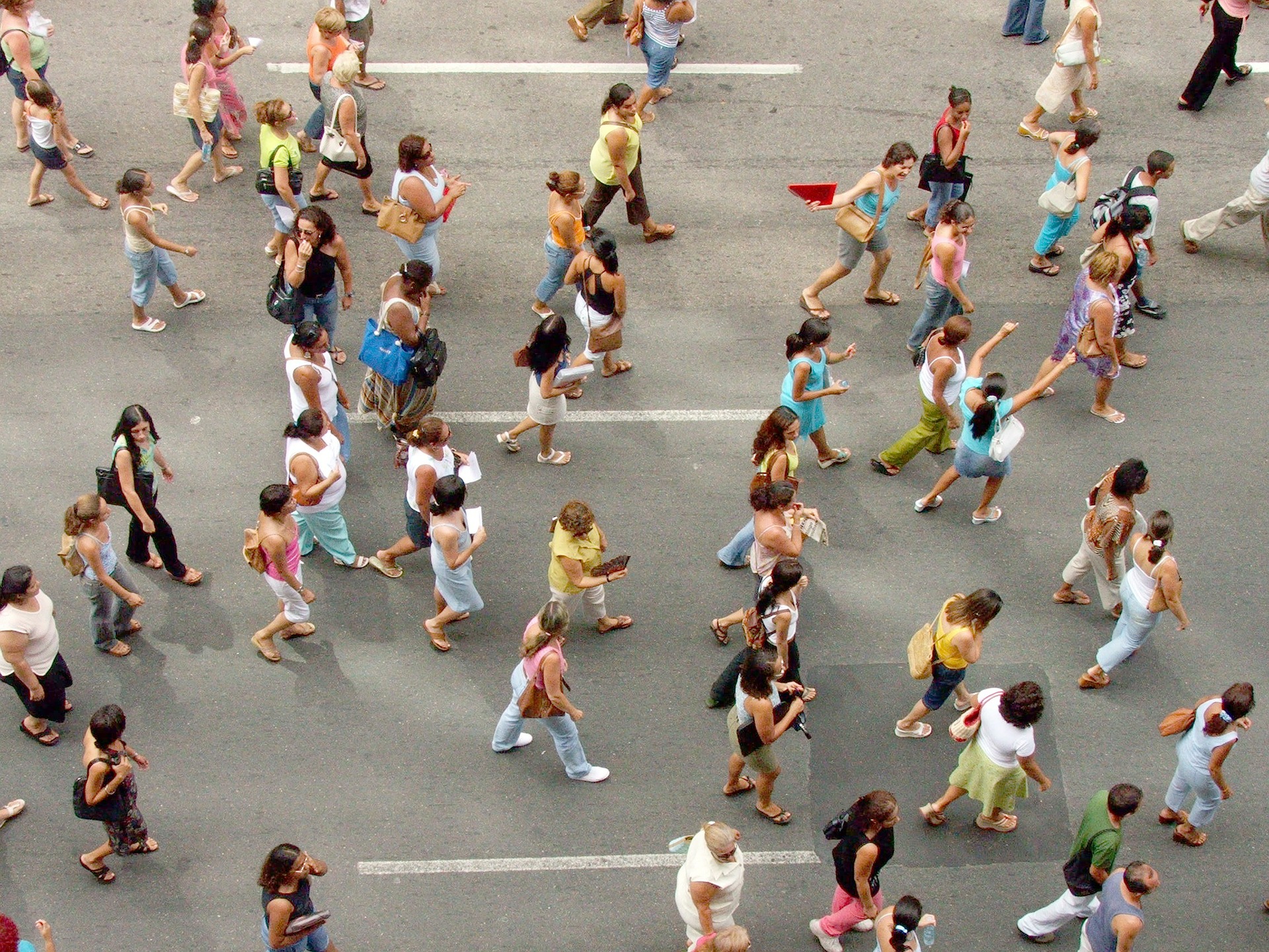 Foto de cima de aproximadamente trinta pessoas caminhando na rua, na pista onde normalmente transitam carros.