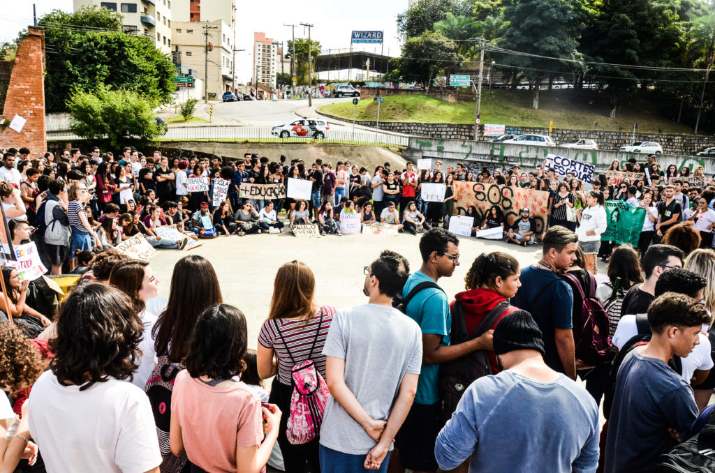 Manifestação com muitos estudantes em roda segurando cartazes de protesto.