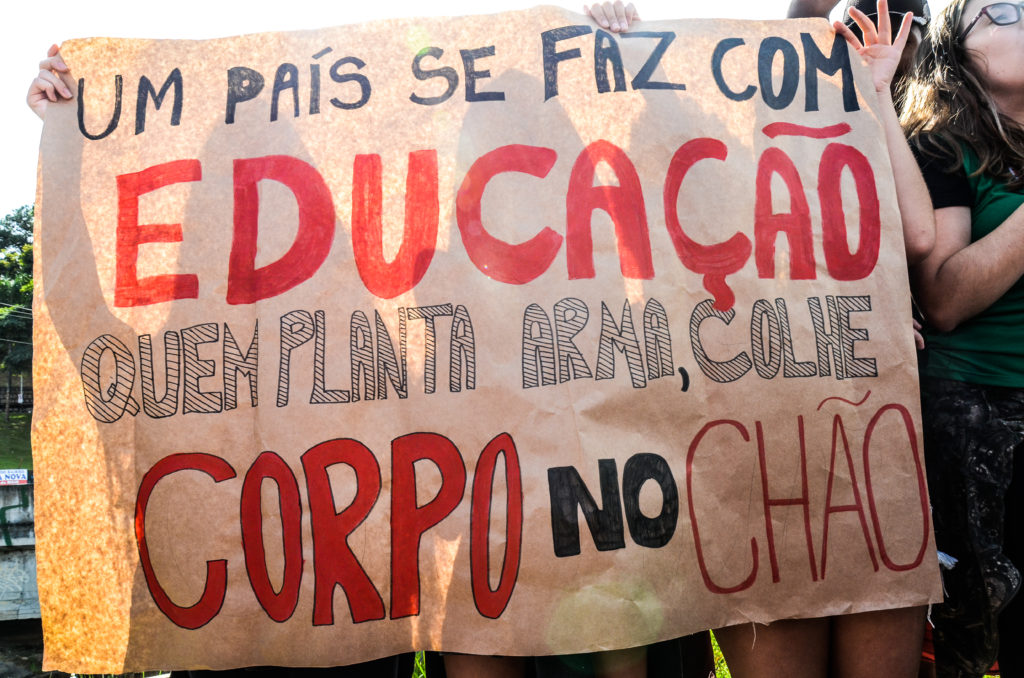 Estudantes segurando um cartaz com a mensagem Um país se faz com educação. Quem planta arma, colhe corpo no chão.