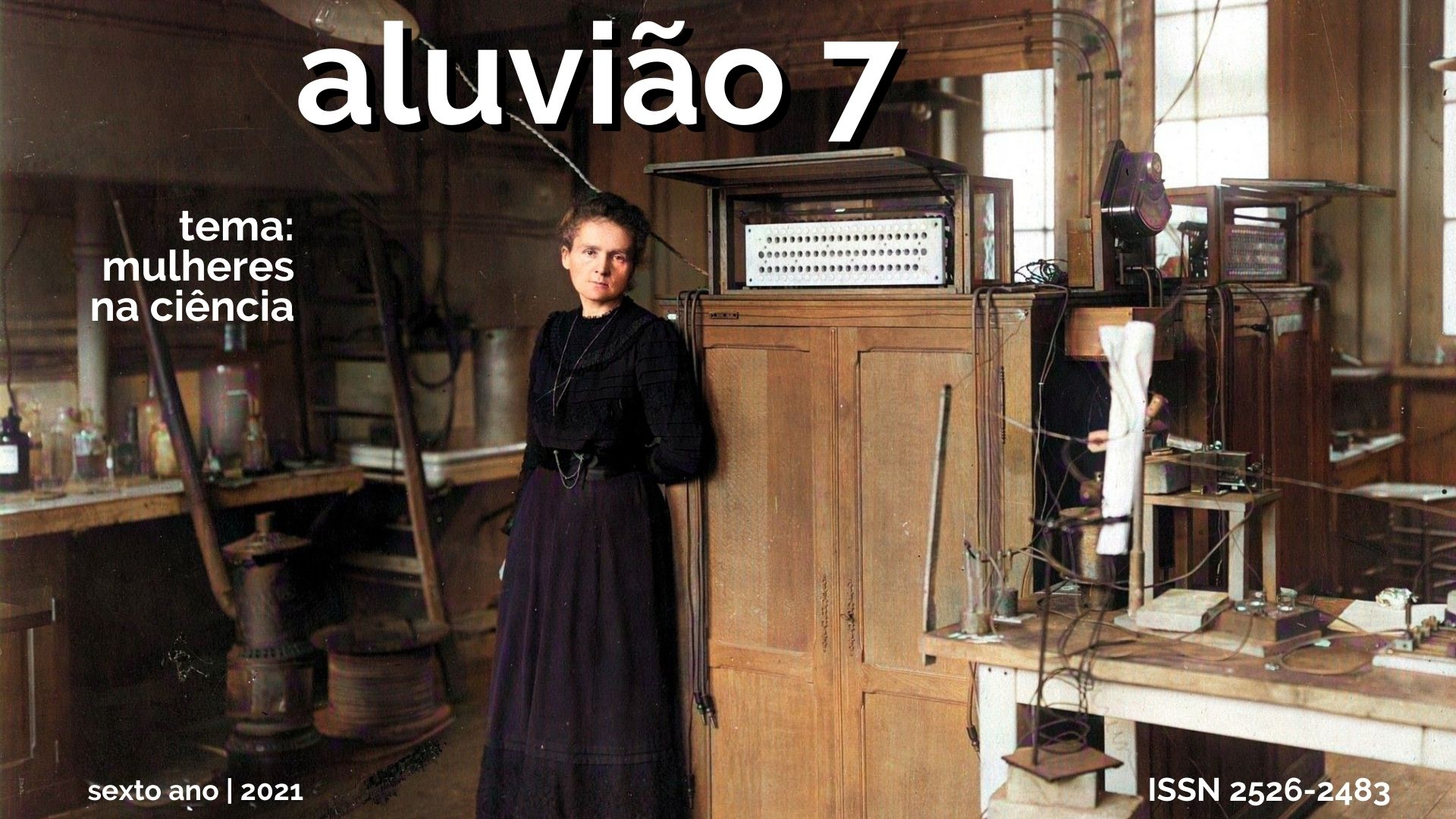 Foto de laboratório de ciências do início do século XX, com a física e química polonesa naturalizada francesa Marie Curie em pé, ao centro, trajando um vestido preto, rodeada por itens de laboratório, como frascos de vidro, lâmpada, mesa e bancada de madeira e gerador de energia elétrica.