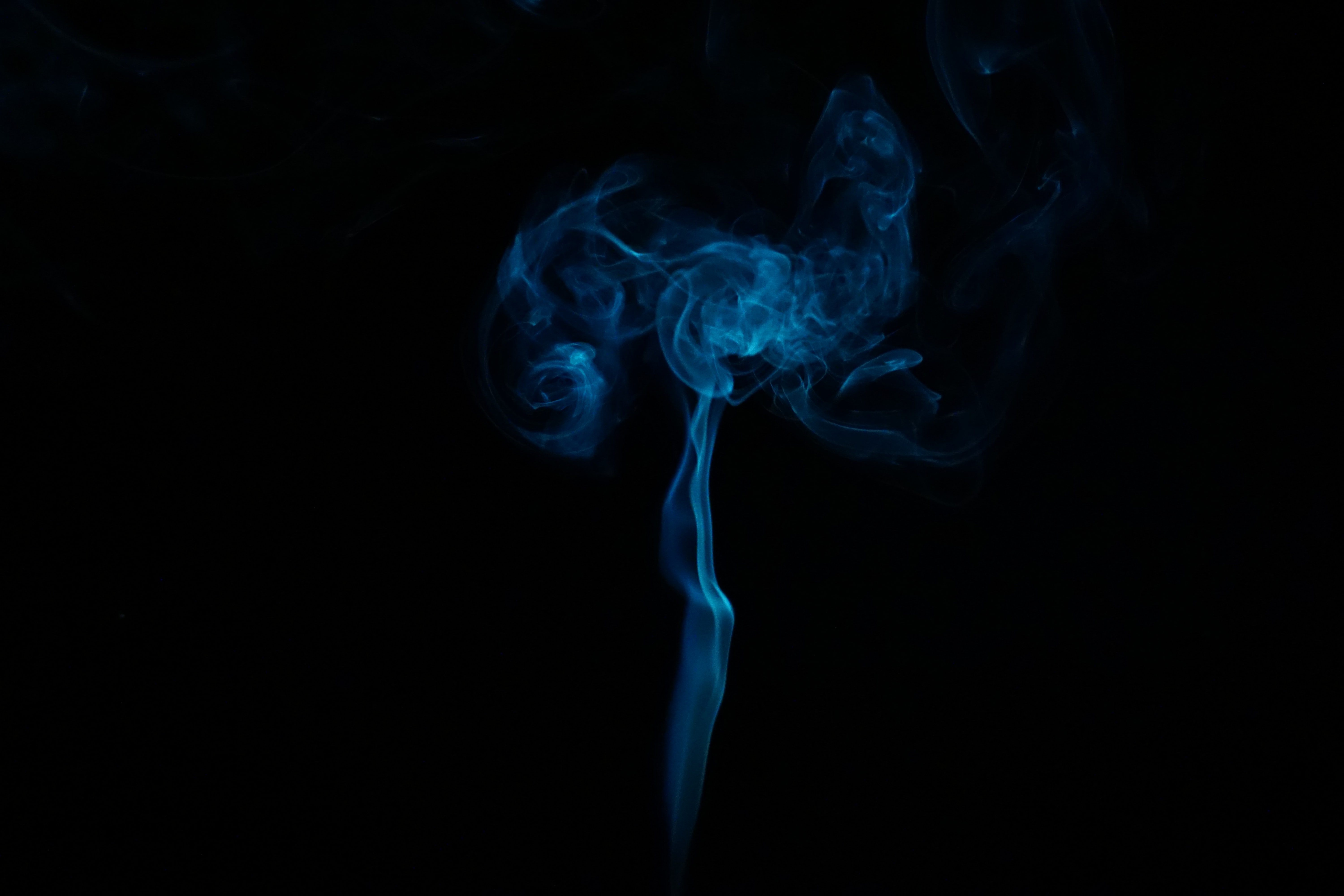Imagem de fundo preto com uma fumaça branco azulada que sai do meio da parte debaixo para cima da foto. A forma da fumaça lembra um cogumelo.