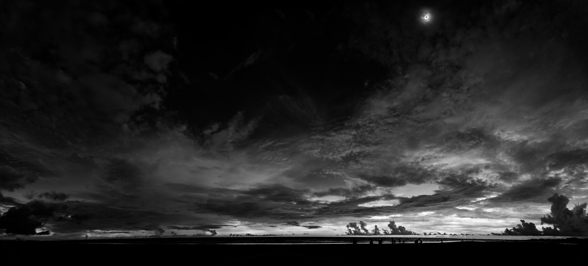 Fotografia de uma paisagem em preto e branco. Mais de noventa por cento da fotografia é o céu com núvens e à direita uma pequena lua.
