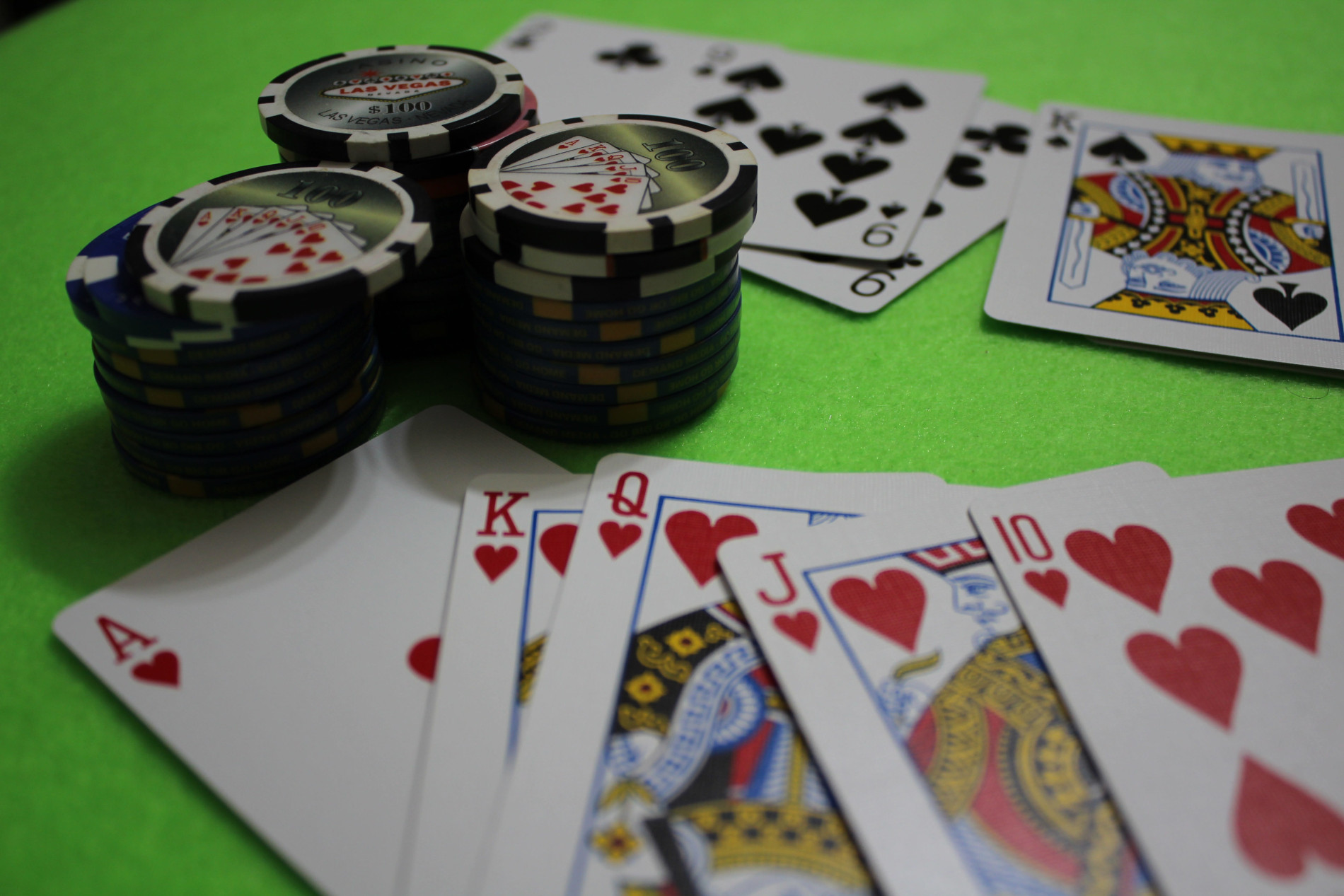 Fotografia de uma mesa verde de jogos de poker com cartas de baralho espalhadas e fichas de jogos;