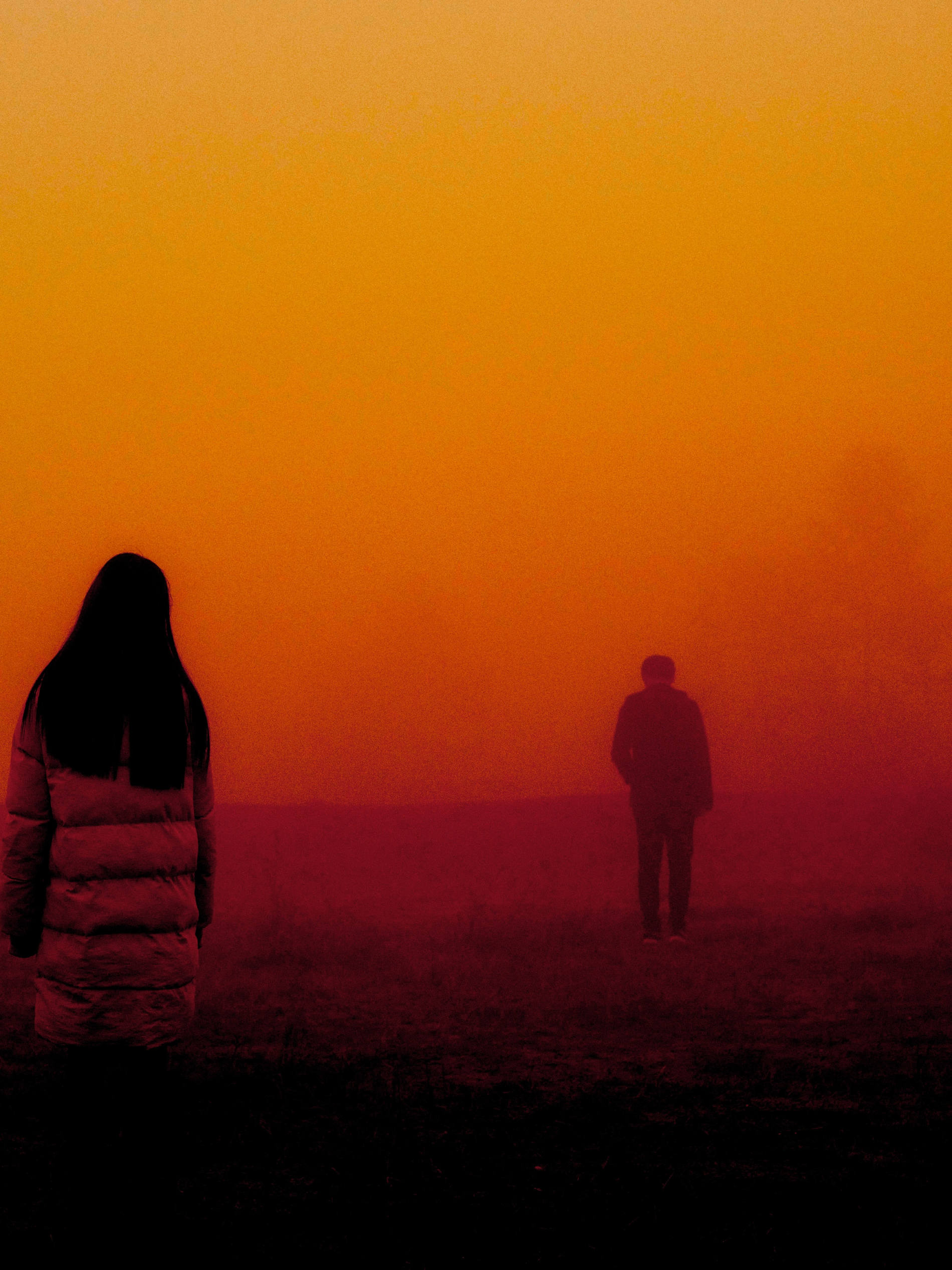 Fotografia conceitual de uma mulher em primeiro plano e um homem em segundo plano, ambos de costas. Em uma atmosfera alaranjada de entardecer.