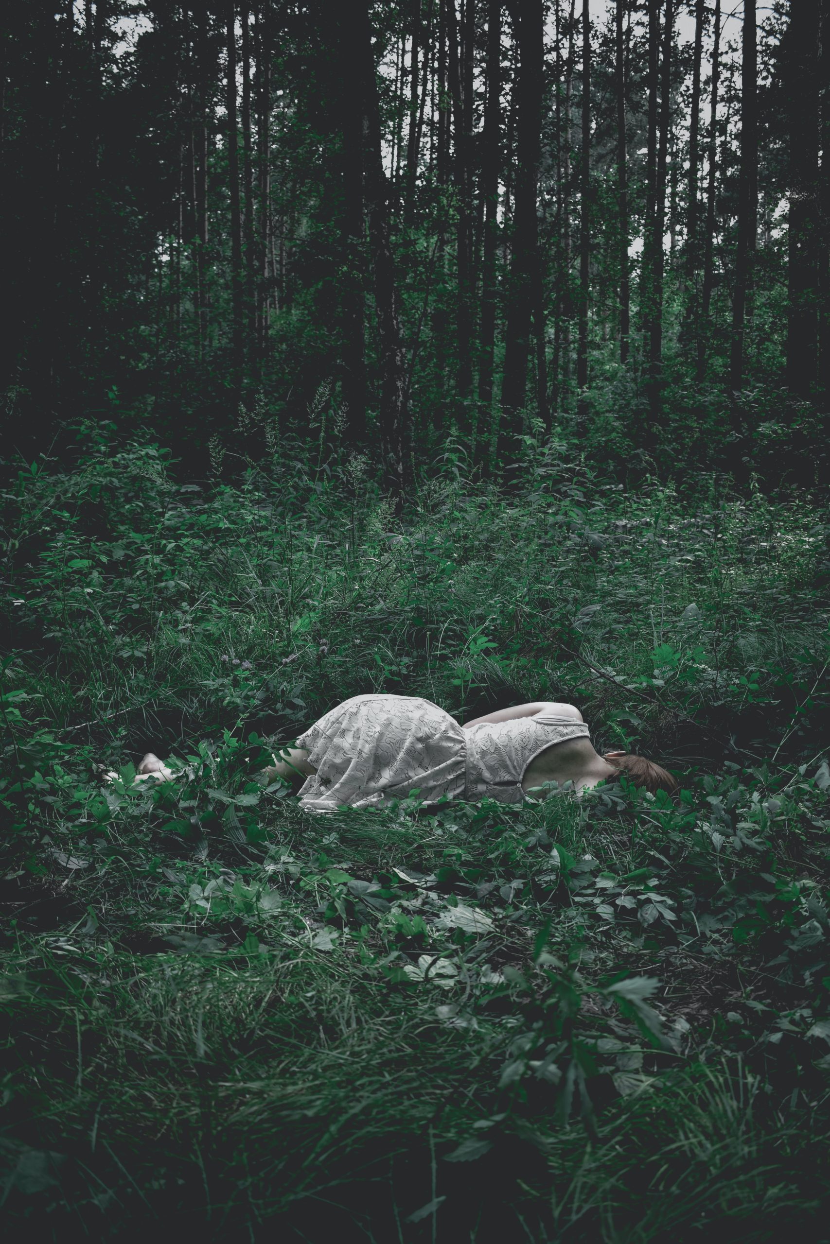 Imagem poética de mulher de vestido branco deitada na grama de costas para o fotógrafo. O ambiente ao redor da mulher é como uma relva densa.