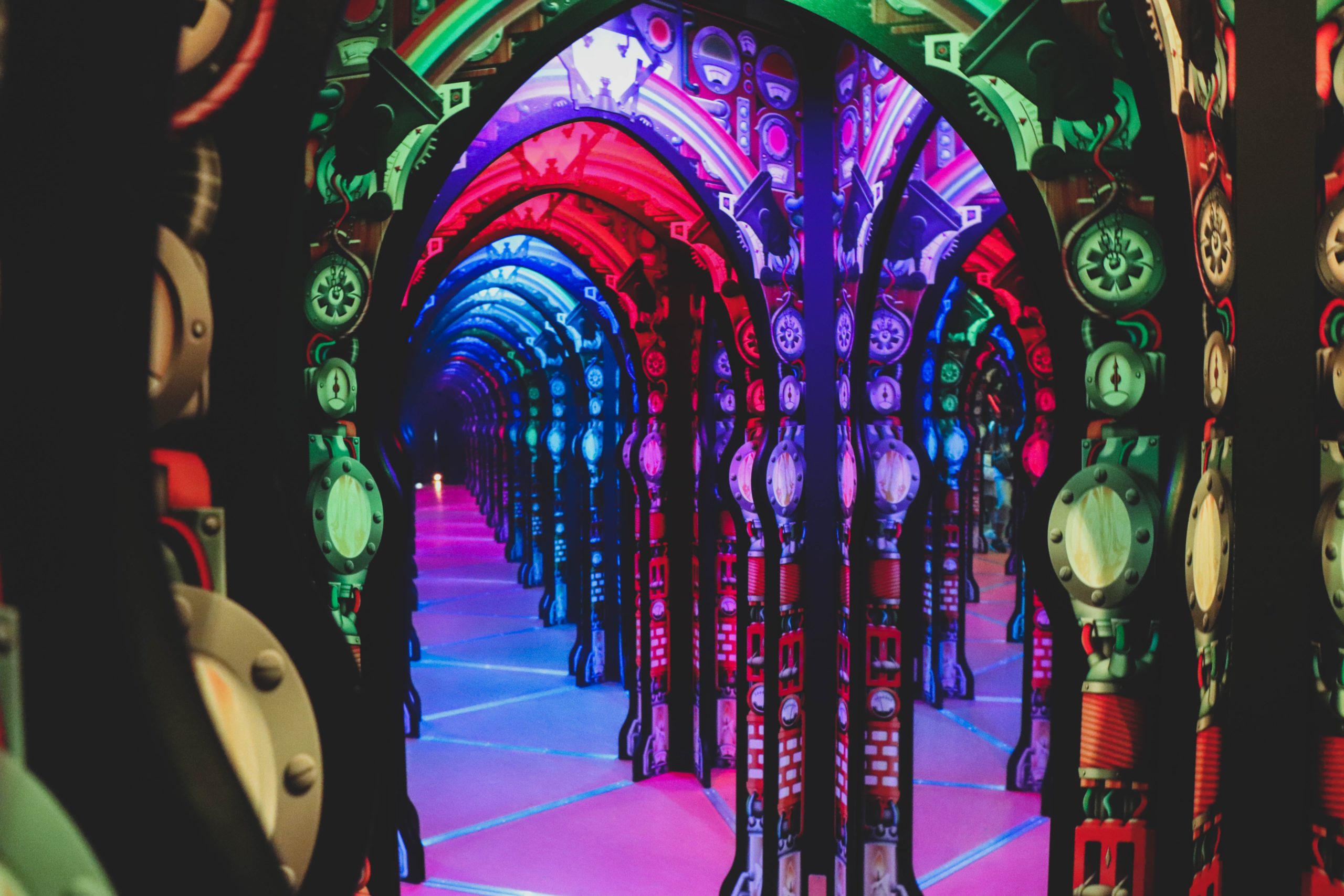 Foto de pavilhão interno do Centro de Ciências de Cingapura. A imagem traz um ambiente multicolorido com vários arcos e espelhos, formando um mosaico de cores vívidas e formas arqueadas.