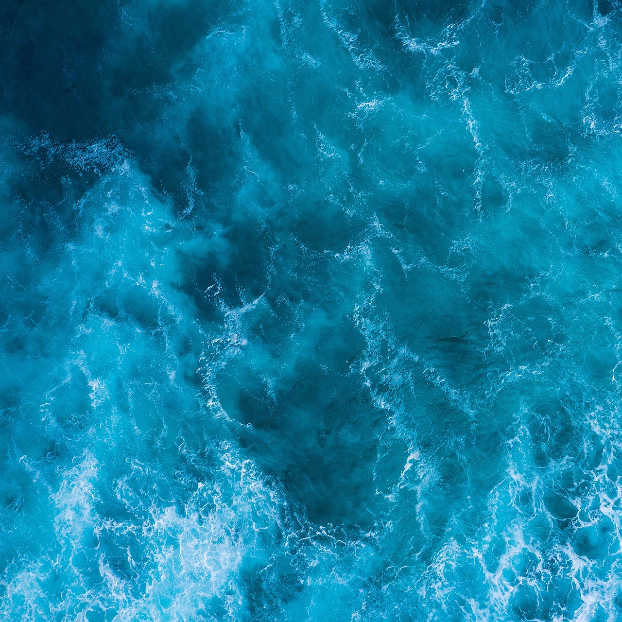 Foto de cima, com visão vertical, de mar azul revolto.