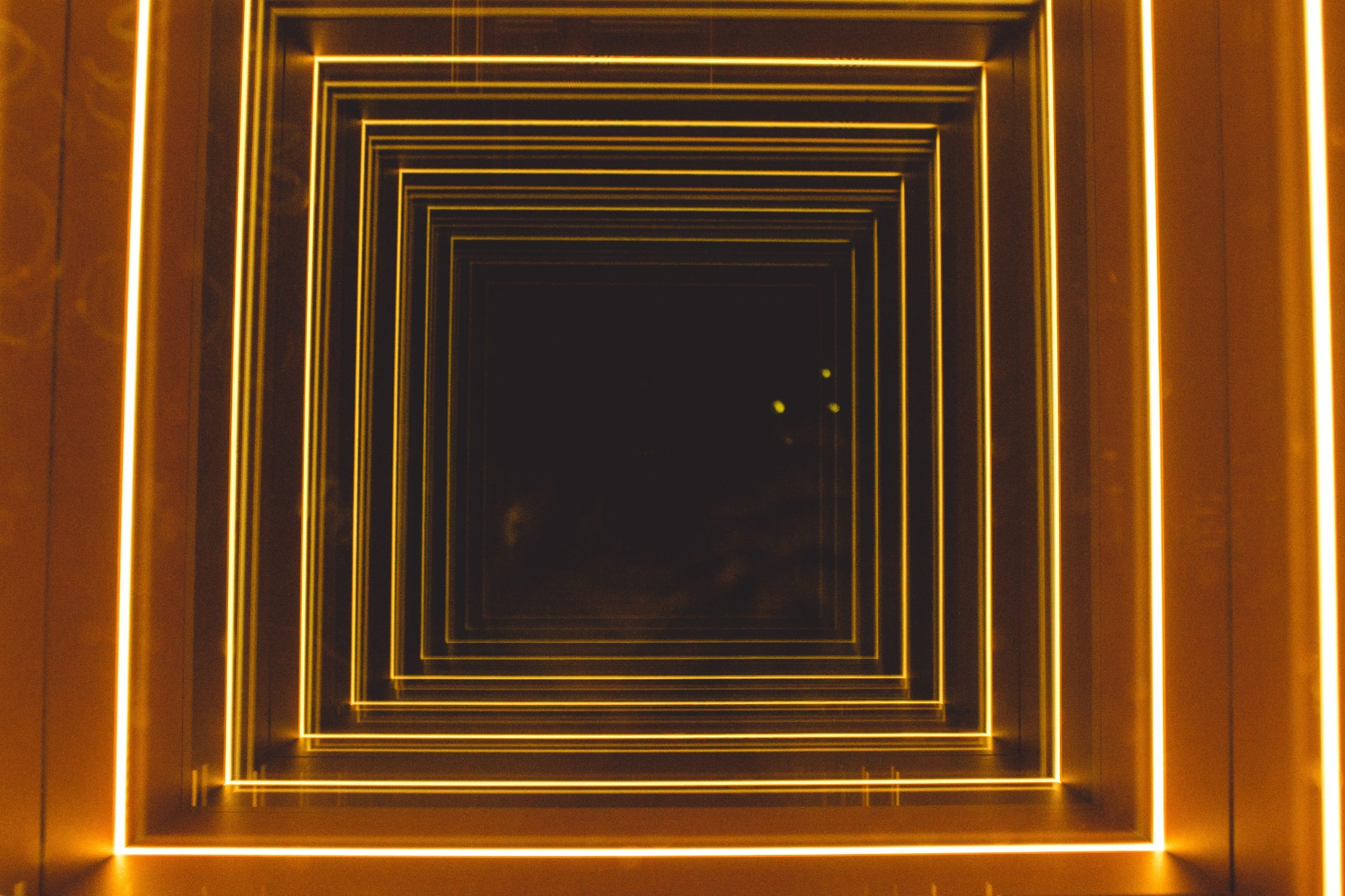 Imagem de um túnel com paredes marrons e vários contornos em neon dourado.