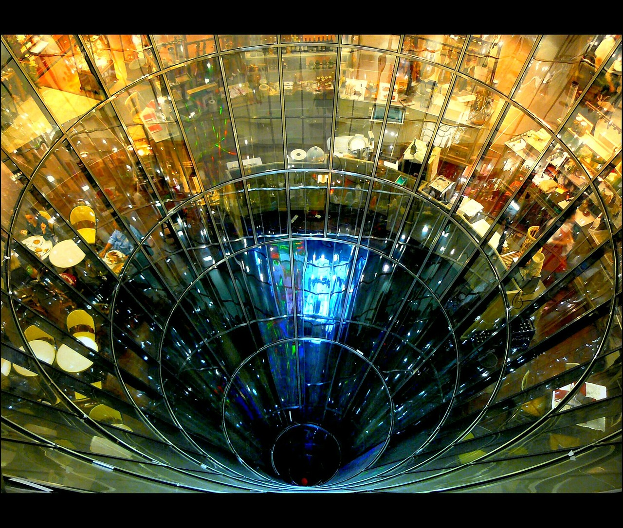 Foto que mostra o vão circular de um edifício de vidro, em que é possível ver mesas de restaurante em um dos andares.