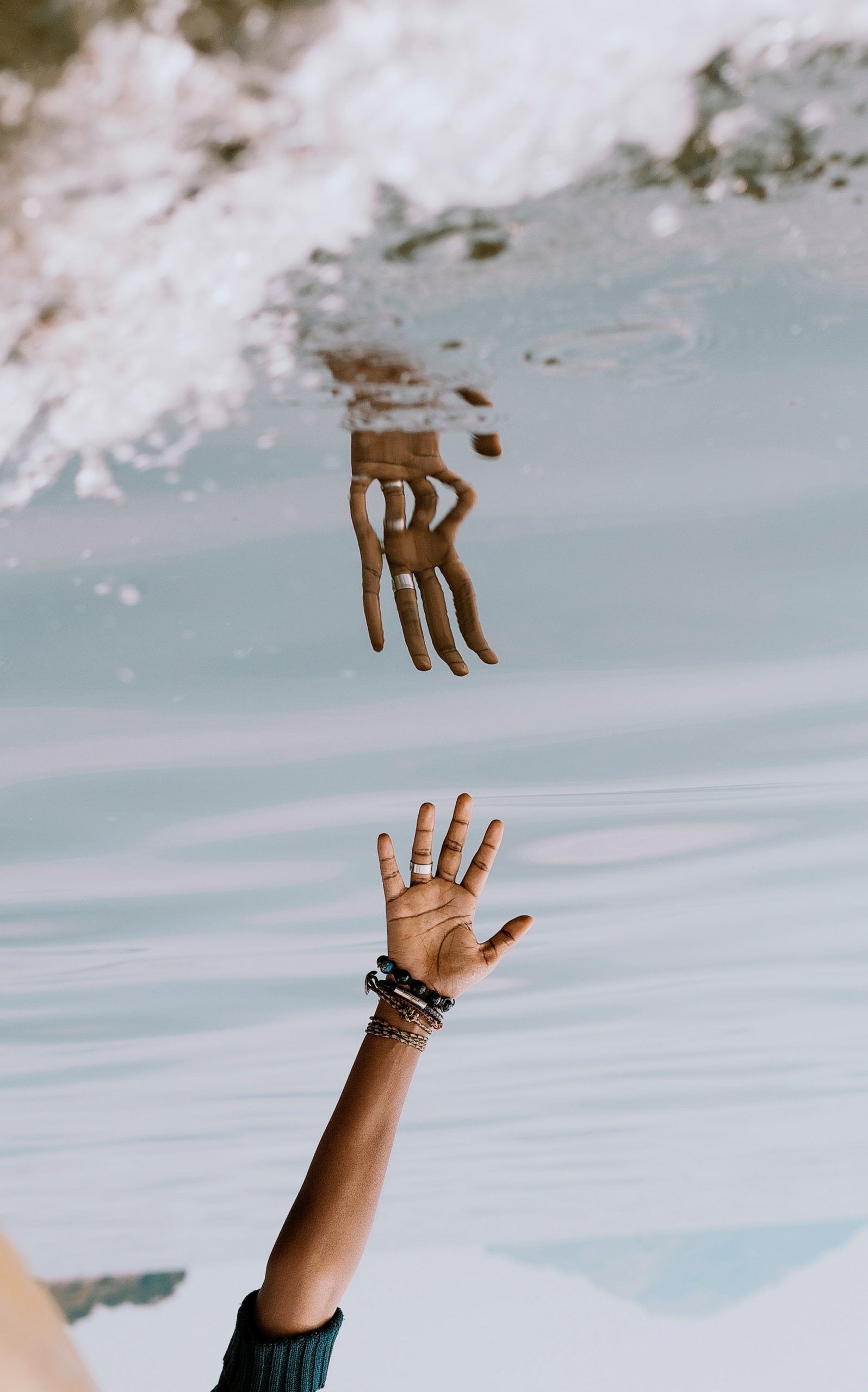 Imagem que retrata uma mão estendida na direção de seu reflexo na água.